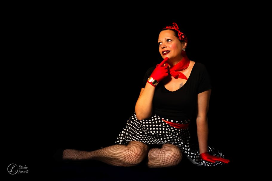 Femme en pose pensante, portant un haut noir, jupe à carreaux et accessoires rouges.