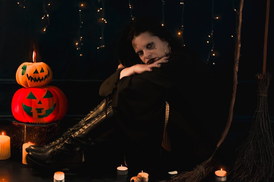 Femme assise près de citrouilles décoratives et de bougies, dans une ambiance mystérieuse.