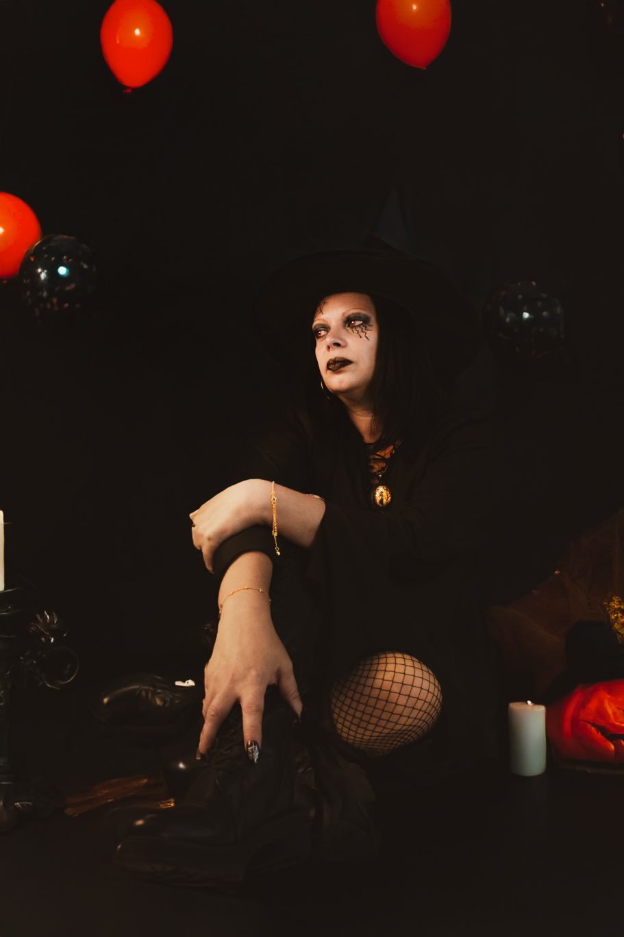 Femme en tenue de sorcière, assise parmi des décorations d'Halloween.