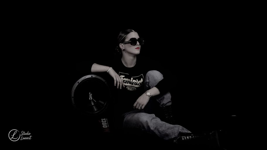 Femme assise, portant des lunettes de soleil, avec un style décontracté dans une ambiance sombre.