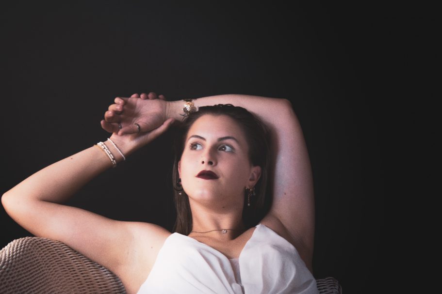 Femme en robe blanche, assise sur un canapé, avec une pose contemplative et élégante.