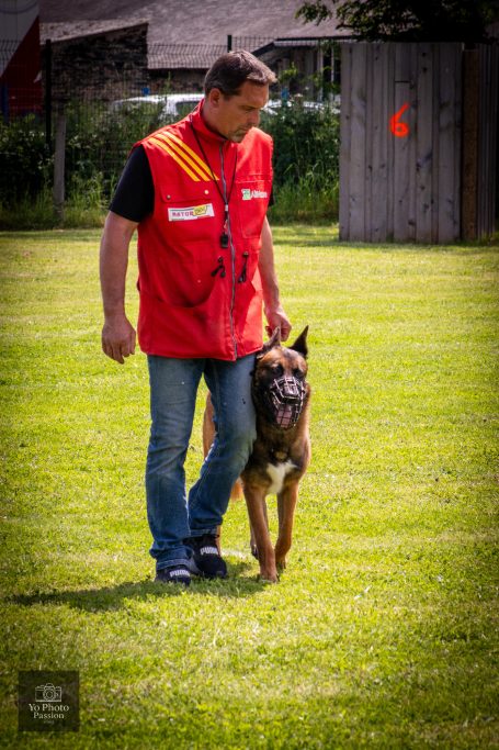 Un homme en gilet rouge marche avec un chien sur un terrain vert.